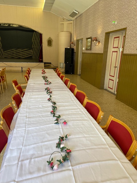 Juhlasalin pöytärivi kohti näyttämöä ja samettiesirippua